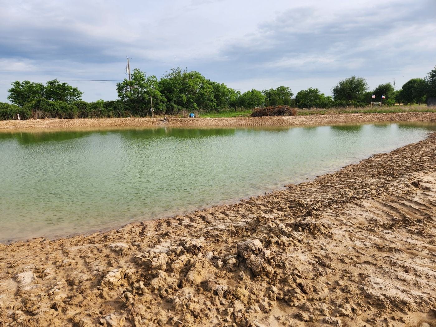 A newly dug pond holding water, with fresh-cut banks in the foreground.